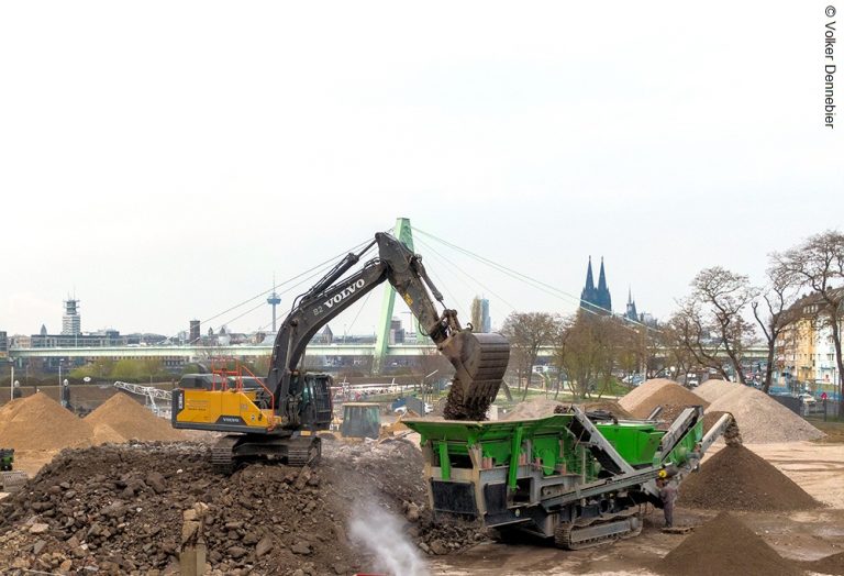 Bagger beschickt Brechanlage zur Aufbereitung von Abbruchmaterial im Deutzer Hafen Köln.