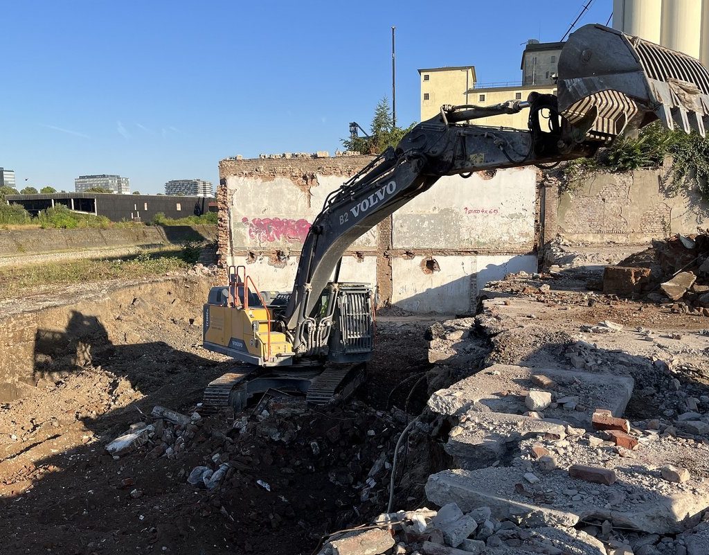 Bagger bei weiteren Rückbauarbeiten auf dem Mühlenareal im Deutzer Hafen Köln entlang des Hafenbeckens.
