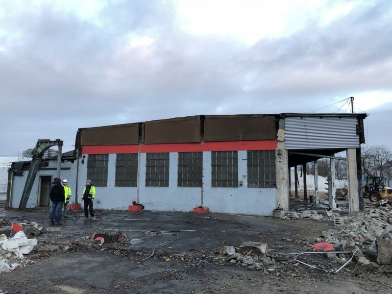 Teilabriss einer Industriehalle im Deutzer Hafen Köln, drei Personen mit Schutzkleidung stehen vor dem beschädigten Gebäude, Trümmer liegen auf dem Boden.