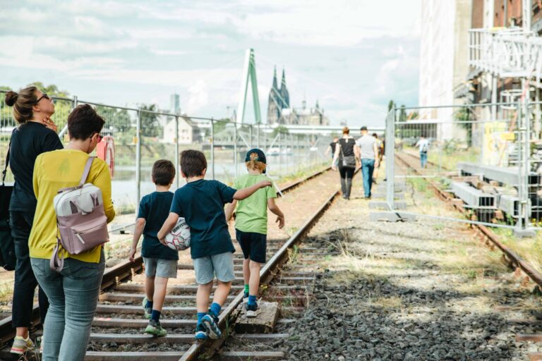 Familien mit Kindern laufen beim Hafentag 2023 über die alten Gleise im Deutzer Hafen. Im Hintergrund sind der Kölner Dom und die Severinsbrücke zu sehen.